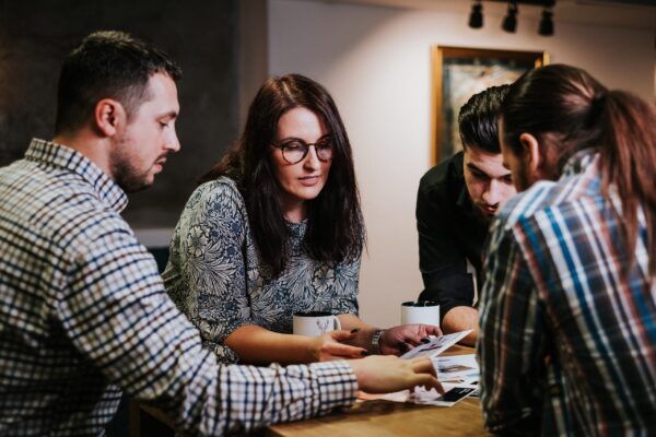 three men and a woman chat over coffee while looking at documents during a meeting